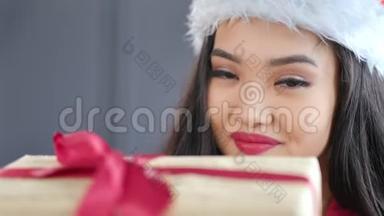 戴着圣诞老人帽子、戴着红蝴蝶结礼品盒的迷人的亚洲小圣诞女孩